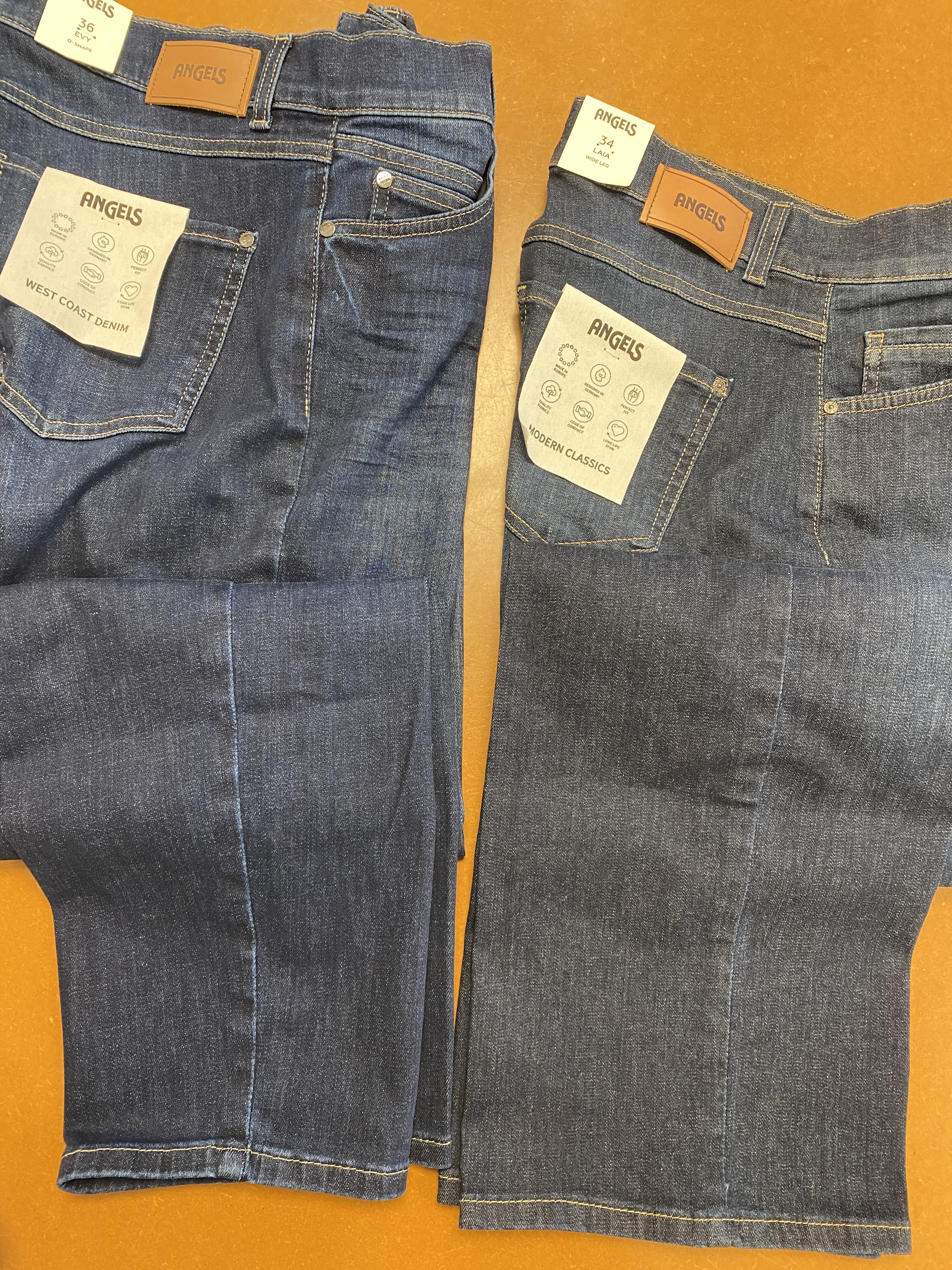 Zwei blaue Angels Jeans mit Etiketten liegen auf orangefarbenem Untergrund