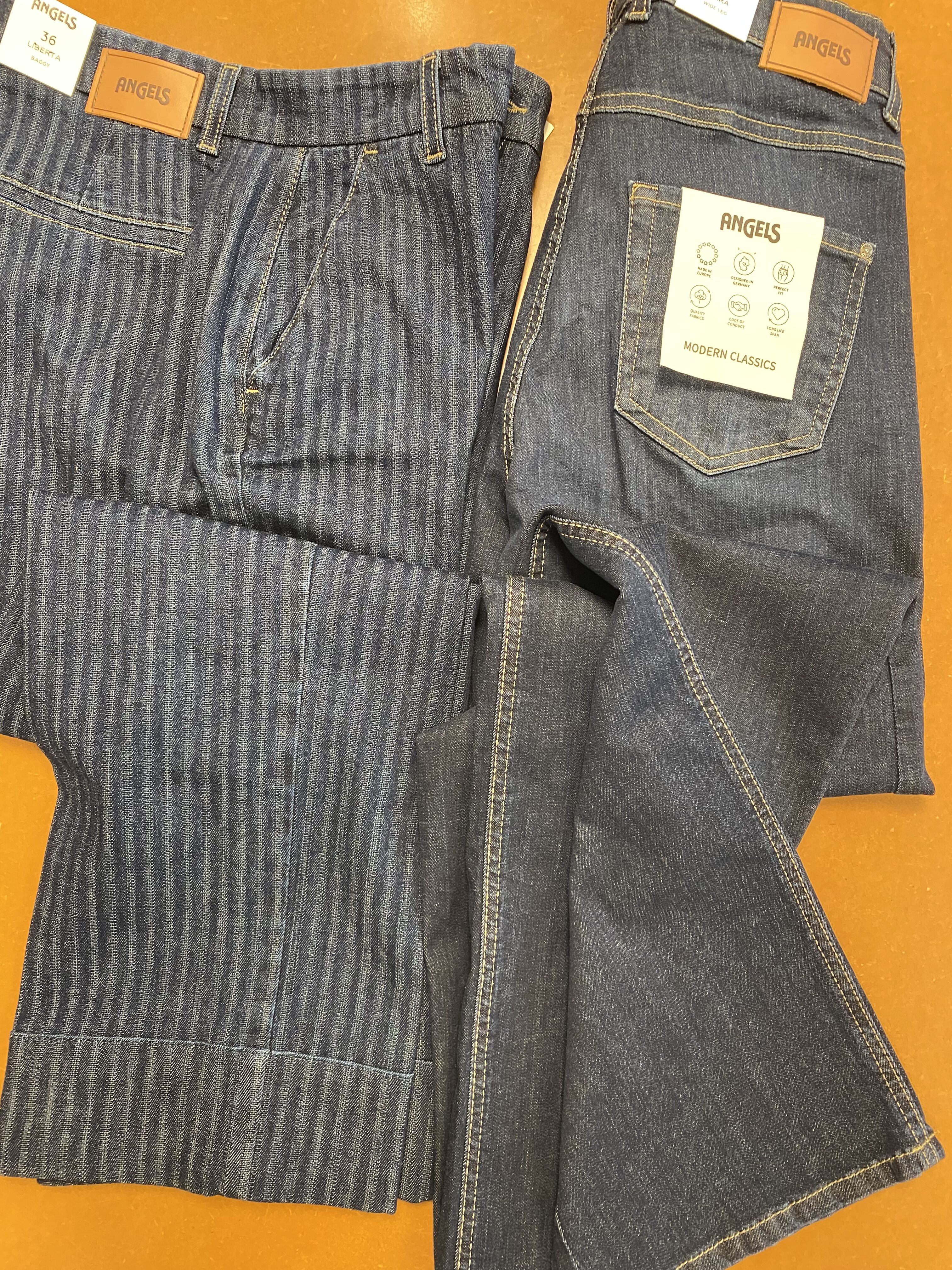 Zwei dunkelblaue Angels Jeans mit Lederlabel liegen auf orangem Untergrund