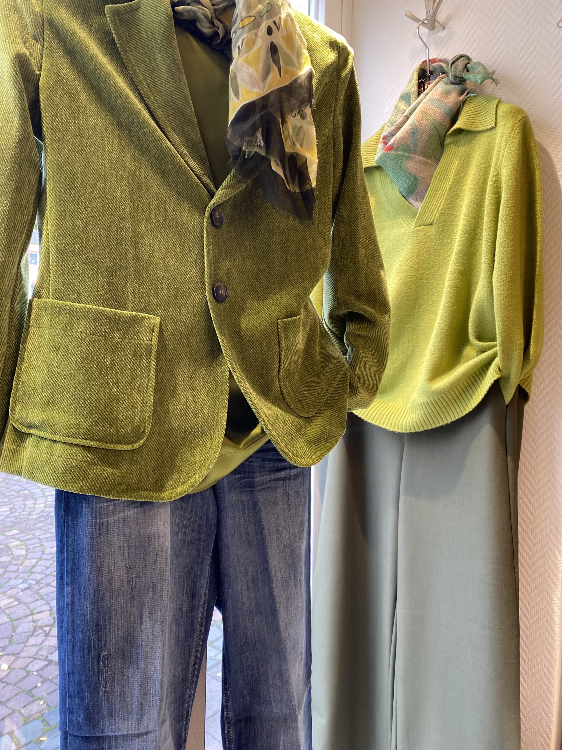 Zwei grüne Outfits mit Blazer Pullover Schals und Jeans im Schaufenster